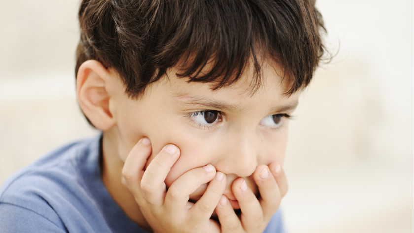 Niño con expresión de enojo y con manos en la boca.